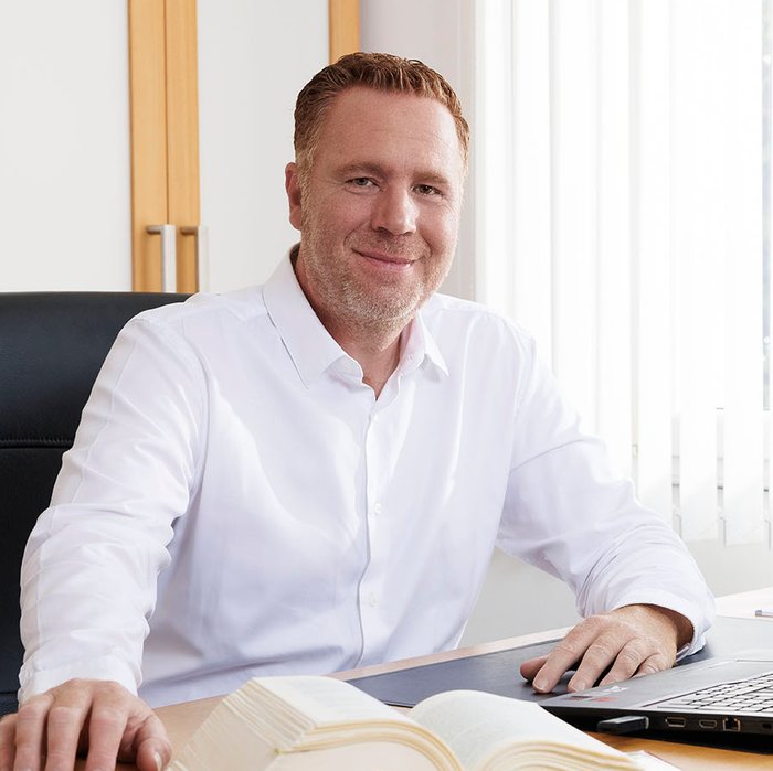 Steuerberater Michael Boos sitzt an seinem Arbeitsplatz in der Kanzlei Hersbruck und lächelt in die Kamera